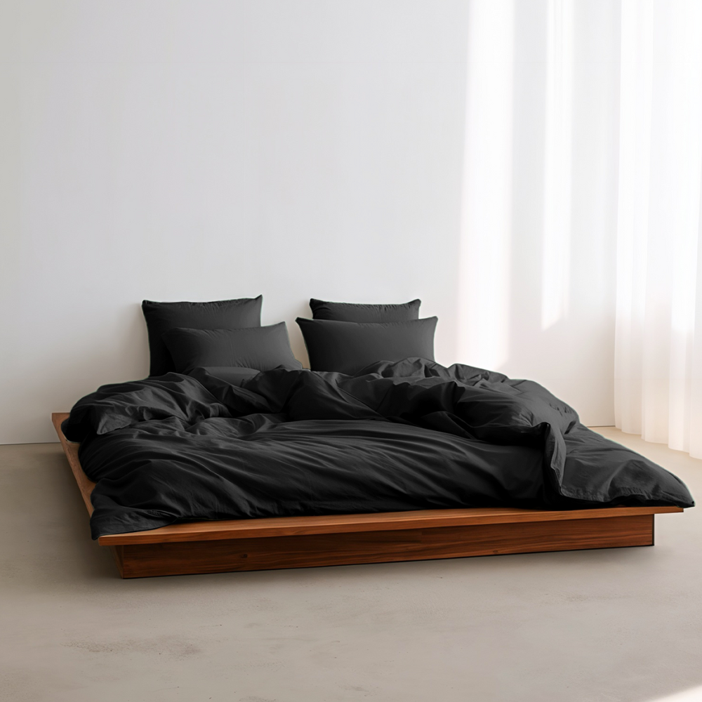 Bed with black bedding and pillows in a minimalistic room.