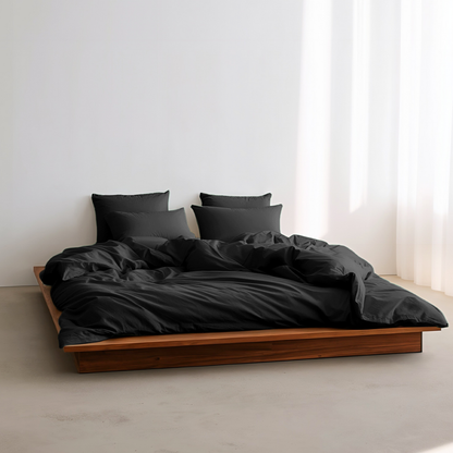 Bed with black bedding and pillows in a minimalistic room.