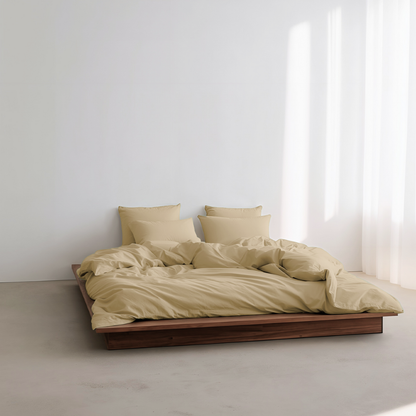 Beige bedding set on a wooden bed against a white wall with a window.
