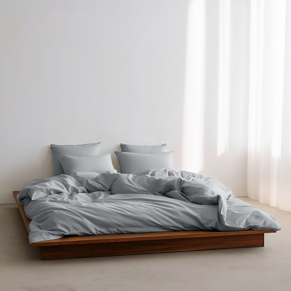 Bed with gray bedding and pillows in a minimalistic room with white walls and curtains.