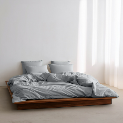 Bed with gray bedding and pillows in a minimalistic room with white walls and curtains.