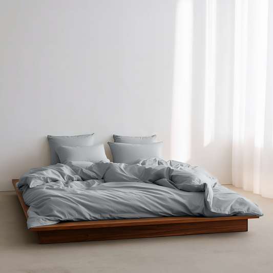 Bed with gray bedding and pillows in a minimalistic room with white walls and curtains.