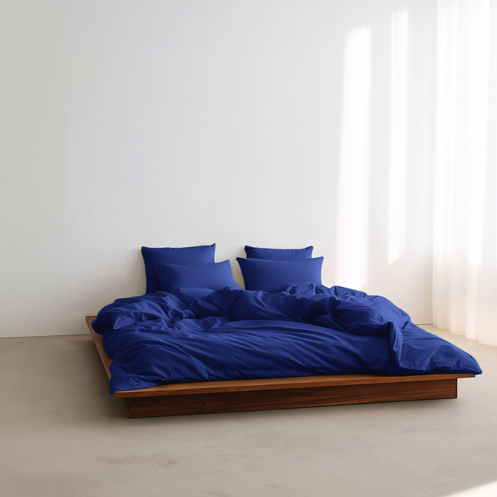Blue bedding set on a wooden bed against a white wall with a window.